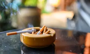 Cenicero lleno de colillas, con un cigarrillo encendido y humo. Un recordatorio de la necesidad de eliminar olor tabaco casa.