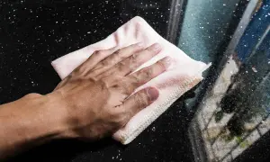 Mano limpiando una superficie de mármol negro con un paño rosa.