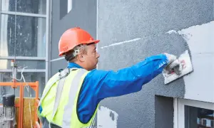 Obrero con casco naranja aplica mortero para como aislar una fachada exterior.