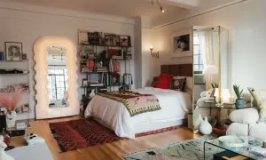 Un dormitorio con un diseño estudio moderno. Cama blanca, estanterías llenas de libros, un espejo ondulado y alfombras coloridas.