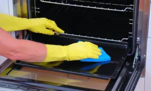 Manos con guantes amarillos limpiando el interior de un horno con una esponja azul.