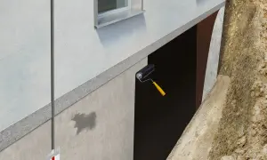 Aplicación de rodillo para impermeabilizar muros enterrados. Se ve la protección de la pared y la tierra excavada.