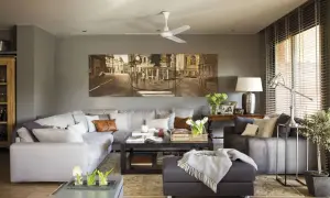 Salones en gris y madera oscura, con un gran sofá modular, mesa de centro y un cuadro de paisaje urbano.