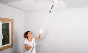 Mujer pintando el techo con rodillo. La pregunta de si que se pinta primero el techo o las paredes es clave en esta tarea.