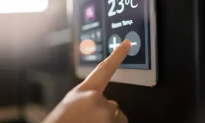 Dedo tocando el botón de menos en un termostato digital que muestra 23°C. Aprende como programar un termostato digital.