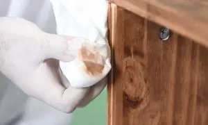 Mano enguantada limpia madera con trapo, eliminando restos para decapar madera y prepararla para un nuevo acabado.