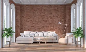 Un salón moderno con una imponente pared de ladrillo visto, sofá blanco, sillón y plantas verdes.