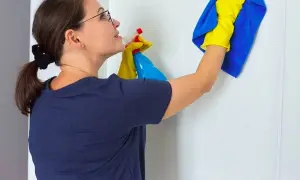 Mujer con guantes amarillos y paño azul limpiando puerta lacada en blanco con spray.