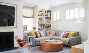 Un salón moderno y acogedor con un sofá rinconera gris, cojines coloridos y un puf de cuero. Ideal para decorar salón con sofá rinconera.
