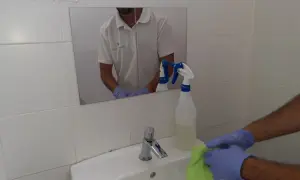 Man con guantes limpia lavabo con paño verde. Spray de limpieza cerca. Aprende como limpiar azulejos baño.