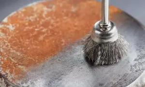 Cepillo metálico eliminando óxido de una superficie. Demuestra cómo quitar el óxido del metal, dejando una zona limpia y brillante.