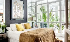 Dormitorio de matrimonio moderno con manta peluda y arte abstracto. Las ultimas tendencias en decoracion de dormitorios de matrimonio se reflejan en la luz natural y las plantas.
