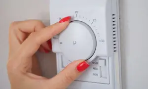 Mano ajustando el termostato para saber como poner la calefacción en casa. La temperatura se marca en grados Celsius.