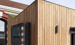 Detalle de una fachada ventilada de madera que contrasta con una pared antigua de ladrillo y piedra.