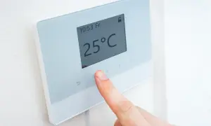 Un dedo ajusta la temperatura en un termostato digital que muestra 25°C.