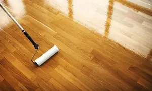 Rodillo aplicando barniz para limpiar suelo madera. El brillo refleja la luz.