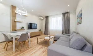Elegante salón con sofá gris, mesa de comedor blanca y detalles en madera. Los colores del salón crean un ambiente acogedor y moderno.