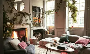 Acogedor salón decorado de Navidad con chimenea encendida, árbol y guirnaldas verdes colgando.
