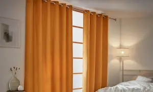 Cortinas aislantes naranjas cubren una ventana, creando un ambiente acogedor. A la izquierda, un cuadro abstracto y un jarrón con espigas.