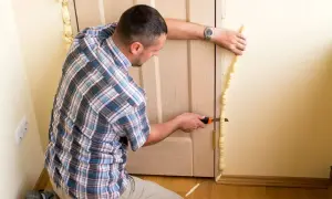 Hombre corta espuma de poliuretano aislante térmico alrededor de un marco de puerta para mejorar la eficiencia energética.