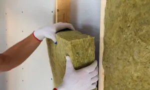 Manos con guantes instalan aislamiento en paredes. El aislamiento térmico de paredes tiene un precio competitivo.