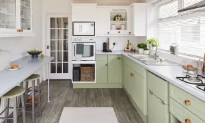 Cocina renovada con gabinetes verdes, encimeras grises y electrodomésticos blancos. Un espacio luminoso y funcional para tu reforma cocina.