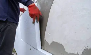Man con guantes naranjas coloca poliestireno para aislar fachadas.