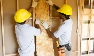 Dos obreros instalan materiales aislantes en una pared de construcción.