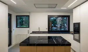 Moderna cocina con isla central de mármol negro y madera. Encimeras a juego, electrodomésticos integrados y grandes ventanales.