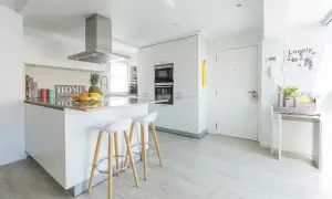 Cocinas modernas blancas con isla central, taburetes y electrodomésticos integrados. Un espacio luminoso y funcional.