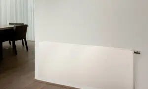 Radiadores de alta temperatura blancos, modernos y discretos, instalados en una pared junto a un suelo de madera y una mesa con sillas.
