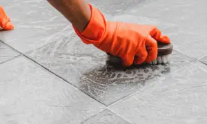 Mano con guante naranja cepillando suelo de terrazo con espuma. Limpiar suelo de terrazo es fácil con esta técnica.