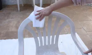 Mano limpiando una silla de plástico blanco con un paño, preparándola para como pintar plástico y darle nueva vida.