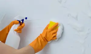 Manos con guantes naranjas rociando y limpiando paredes con espuma y esponja.