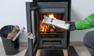 Persona con guantes verdes y grises introduce un producto envasado en una chimenea encendida. Es parte de la limpieza de chimeneas.