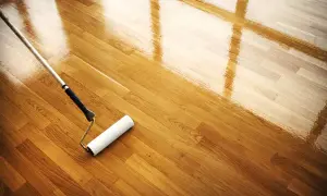 Rodillo aplicando barniz a un suelo de parquet de madera, restaurando su brillo. Mantenimiento parquet.
