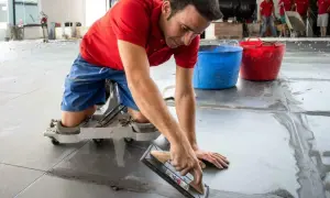 Un trabajador con rodilleras aplica cemento para saber como poner baldosas en el suelo.