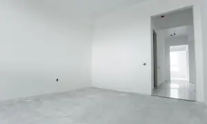 Habitación vacía con paredes blancas y suelo de cemento. El yeso aguanta el calor, preparándose para un nuevo hogar.