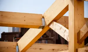 Estructura de vigas de madera clara, parte de techos de madera en construcción, con uniones metálicas visibles.