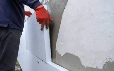 Man con guantes naranjas coloca poliestireno para aislar fachadas.