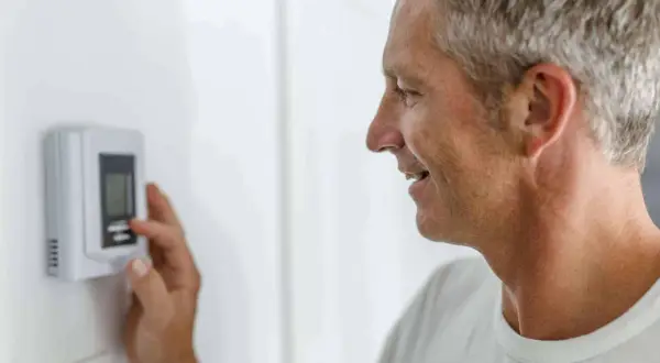 Hombre ajustando el termostato para entender como funciona un termostato de calefacción y mantener la temperatura ideal en casa.
