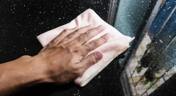 Mano limpiando una superficie de mármol negro con un paño rosa.