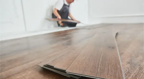 Instalador colocando tablas de vinilo SPC en un suelo de madera.