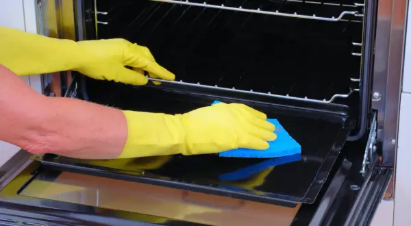 Manos con guantes amarillos limpiando el interior de un horno con una esponja azul.