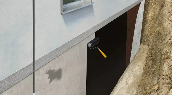Aplicación de rodillo para impermeabilizar muros enterrados. Se ve la protección de la pared y la tierra excavada.