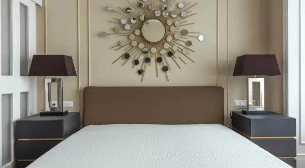Un espejo sol y lámparas oscuras sobre mesitas de noche grises ayudan a alegrar una habitación con muebles oscuros.