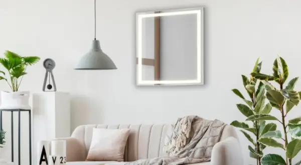 Un espejo iluminado sobre un sofá beige, con plantas y un reloj. Ideas de donde colocar espejos en el salón para ampliar el espacio.