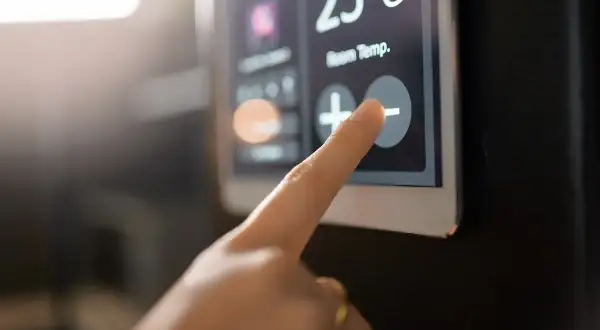 Dedo tocando el botón de menos en un termostato digital que muestra 23°C. Aprende como programar un termostato digital.