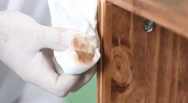 Mano enguantada limpia madera con trapo, eliminando restos para decapar madera y prepararla para un nuevo acabado.