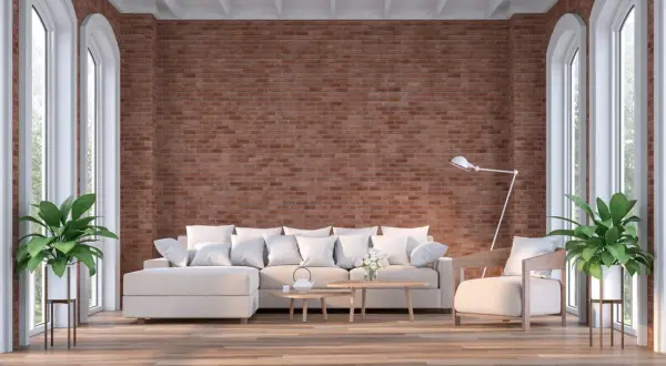 Un salón moderno con una imponente pared de ladrillo visto, sofá blanco, sillón y plantas verdes.